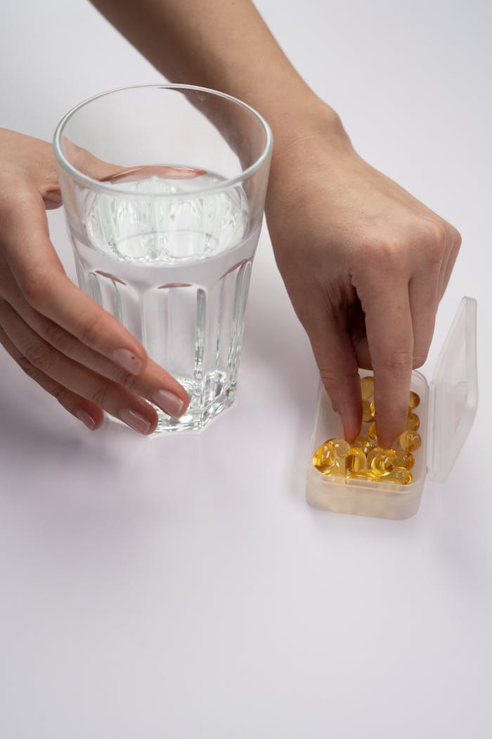 A hand selecting supplements from a pill box beside a glass of water, symbolizing health.
